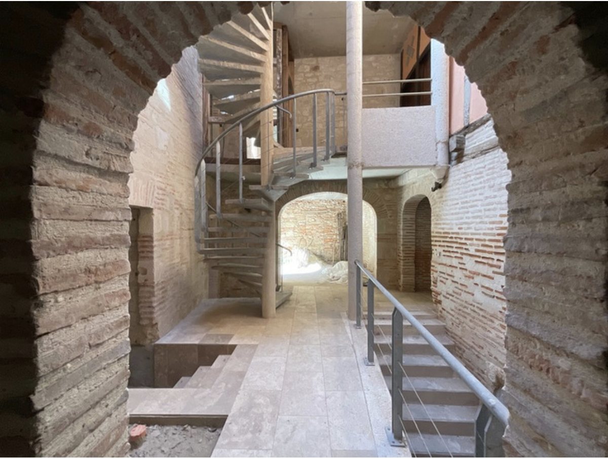 Intérieur de l'immeuble en cours de travaux : arches en brique, escalier hélicoïdal et sols en pierre